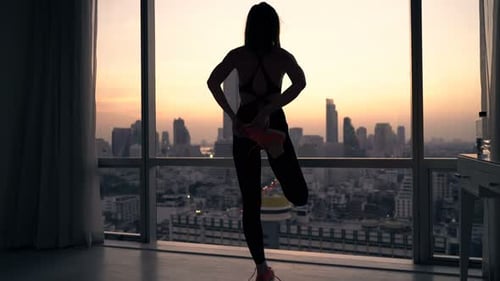Woman Stretching Legs in Apartment Overlooking City Skyline