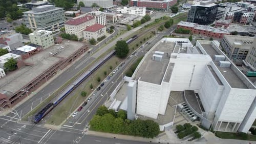 Aerial drone follows train as it rolls out of train station, depot. Urban. Commuter rail.