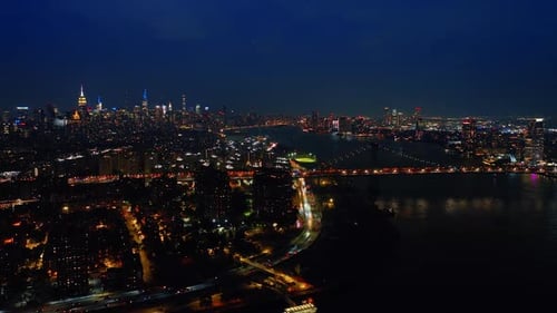 Footage above the dark waters of the East River at night. Luminous cityscape of New York