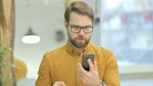Man Looking at Smartphone Celebrates Success