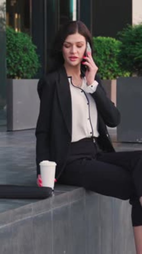 An attractive businesswoman is sitting on the stairs in front of a glass business center.