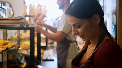 Smiling male and female bakers arranging pastries in a bakery.
