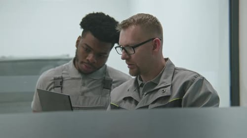Two Men in Work Uniforms Look at Tablet