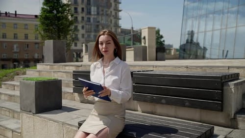 Young Woman Sits Outdoors with Presentation Folder