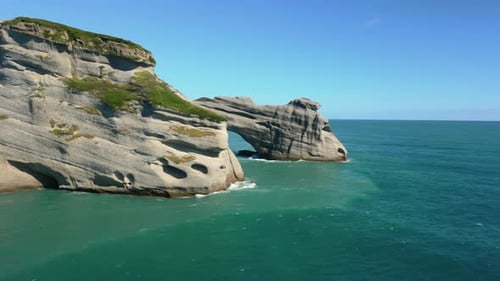 Low flight around tip of sea stack revealing arched stack and Whareriki Beach in background, South I