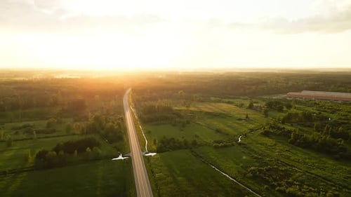 Vista aérea de uma estrada rural vazia ao pôr do sol cercada por campos verdes e terras agrícolas capturadas com um