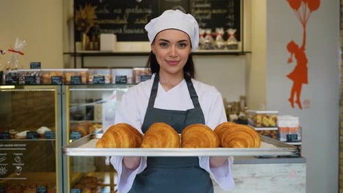 Smiling Baker Woman Holding Croissants in Bakery