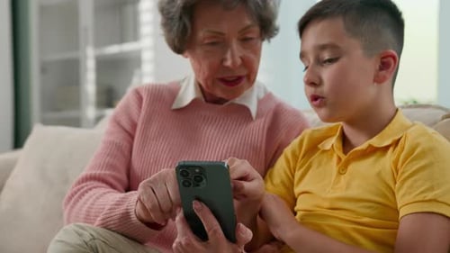 Grandmother and Grandson Using Phone Together on Couch