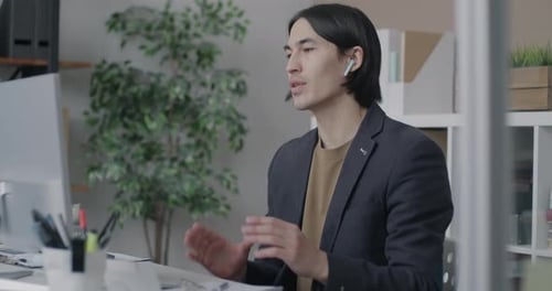 Asian Businessman Making Online Video Call with Computer and Wireless Earphones in Office