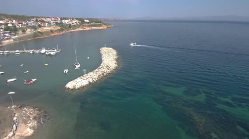 Aerial shot of a small Greek harbor with turquoise and blue waters with fishing boats and craft comi