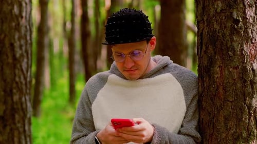 A Man in a Hat and Glasses is Standing in the Forest with Smartphones