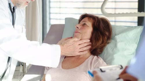 Senior doctor examines woman patient during hospital checkup in private room