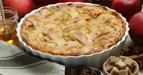 Delicious homemade pie in baking dish, fresh apples and spices spinning on table, closeup