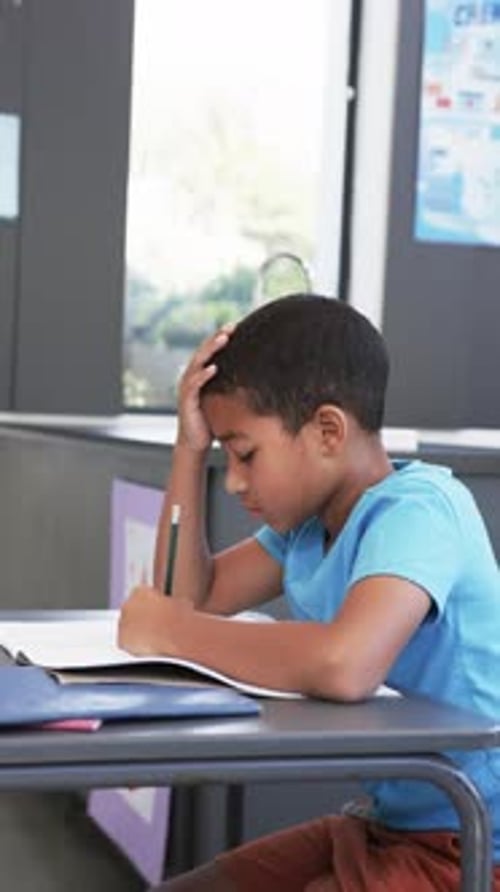 Vertical video: In school, child studying and writing in notebook, concentrating on work
