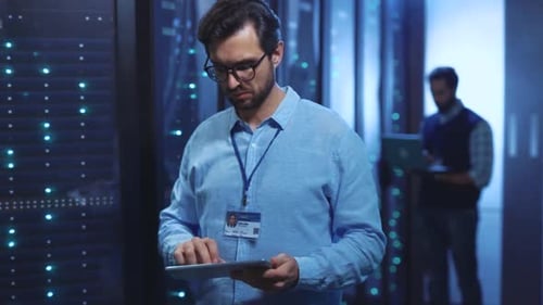 A Man in a Blue Shirt Uses His Tablet to Monitor Servers and Data