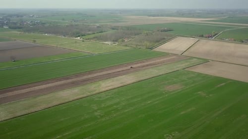 Aerial drone shot over the big wide farm fields with the tractor is moving to plow the ground