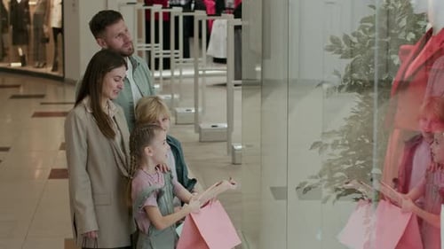 Parents Discussing Trendy Clothes in Showcases when Going Shopping in Mall