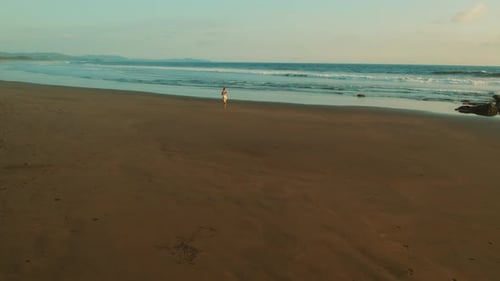Slim woman running on wide sandy beach by the ocean during calm tropical sunset