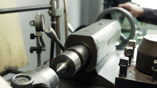 Turner works at a lathe processes the metal part on a lathe in a lathe shop