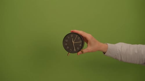 A Hand Holding a Clock Against a Beautiful Green Background for Visual Impact and Appeal