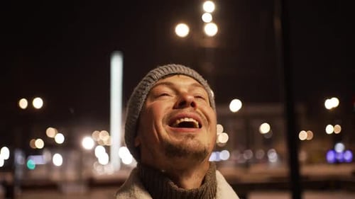 Man Looks Up at Snow Falling in City Night