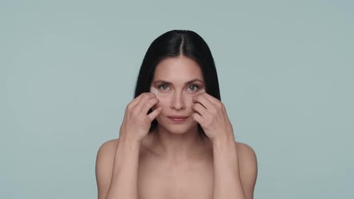 Portrait of a Seminude Woman with Hyaluronic Patches Under Her Eyes on a Blue Background Close Up