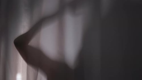 Silhouetted Person with Arms Up Behind Curtain