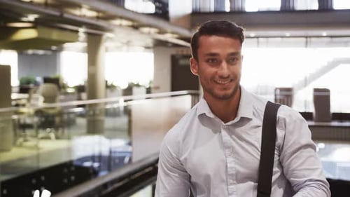 Smiling businessman in office building, carrying bag and looking down