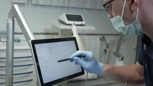A Professional Dentist Man Looks at a 3d Model of Teeth on a Computer Monitor