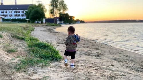 Active Caucasian toddler running by the beach. Happy child plays with sand at the shore at sunset.
