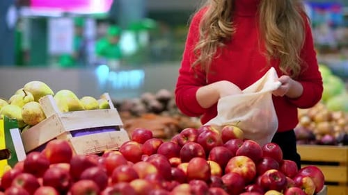 Mujer recogiendo manzanas en una bolsa reutilizable en una tienda. Temáticas del Día de la Tierra y la Ecología