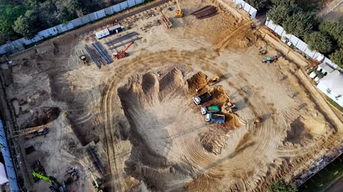 Aerial perspective of heavy operating across a dusty construction zone, with excavated pits, soil