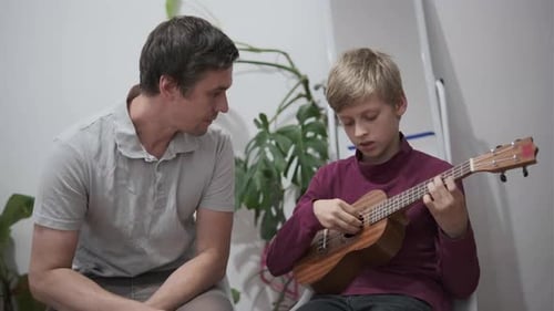 Boy Plays Ukulele as Man Watches