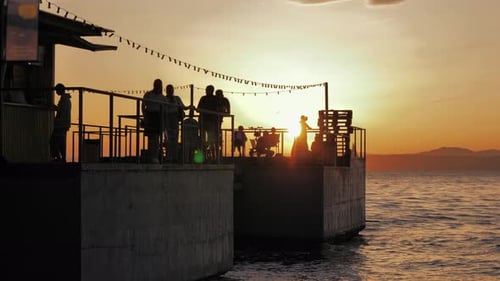 Many People on the Pier Enjoying Orange Sunset Silhouettes of People Against Sunset Sky