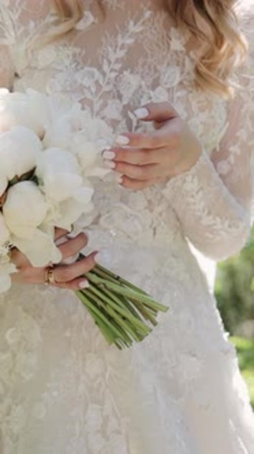 A bride holds wedding flowers bouquet in garden. Charming woman holding leaves and flowers outdoors.