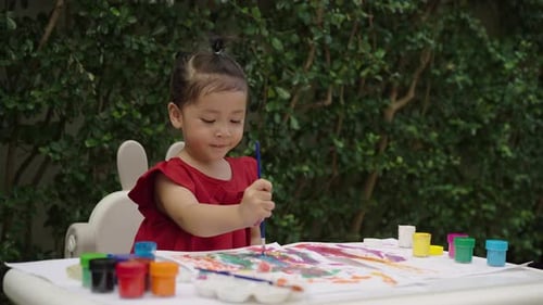 happy toddler girl painting watercolor in a paper at backyard