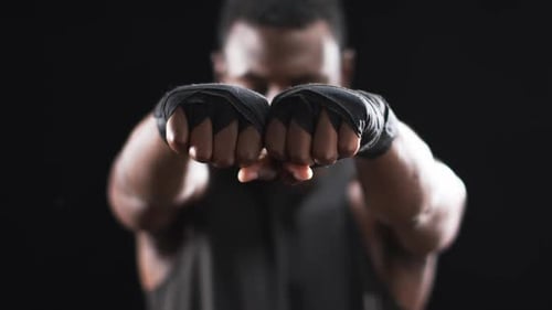 African American boxer shows off boxing gloves on a black background