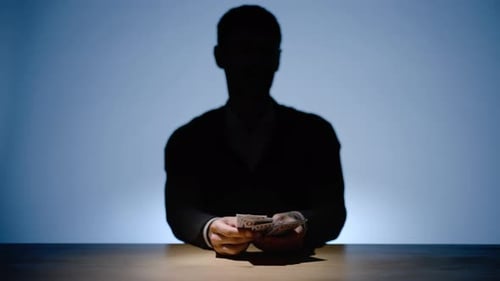Silhouette of Unrecognizable Man Counting US Banknotes Cash Over Wooden Desk