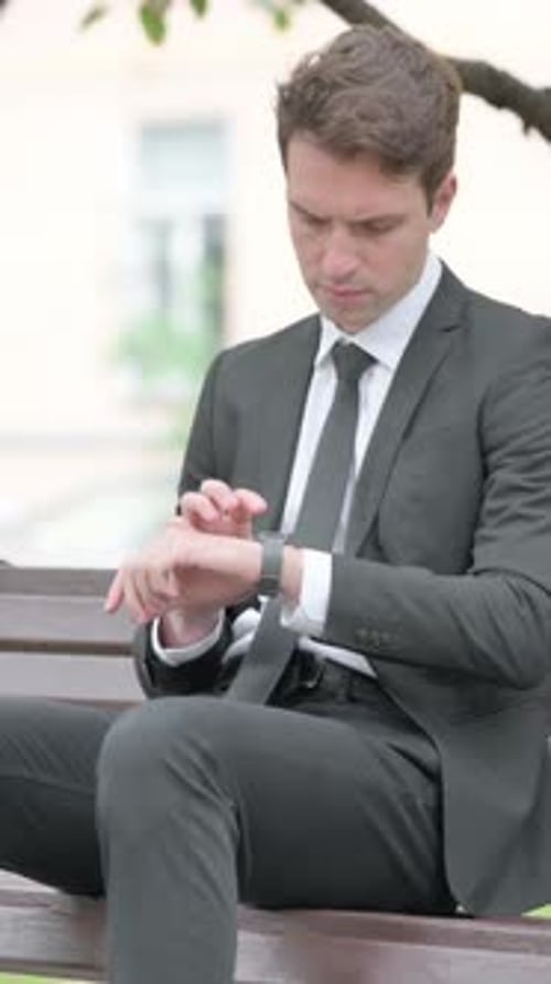 Man in Suit Checking Smartwatch While Sitting on Bench