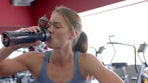 Fit young Caucasian woman hydrates during a gym workout
