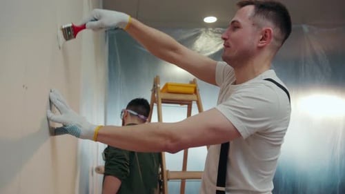 Cheerful Young Builders Actively Paint the Walls of the Apartment Joking and Laughing Positive
