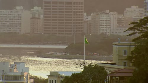 Brazillian flag waving proudly above Rio de Janeiro in golden sunlight