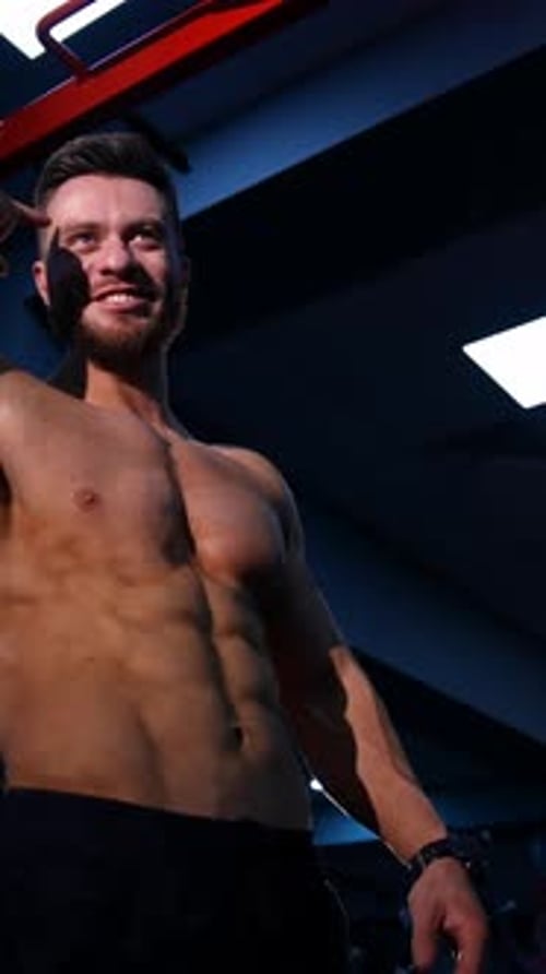 Healthy bodybuilder indoors. Smiling young man with sportive body talking in the modern gym.