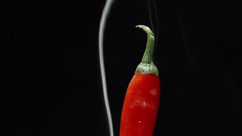 half of the red pepper rotates and smokes on a black background, close-up