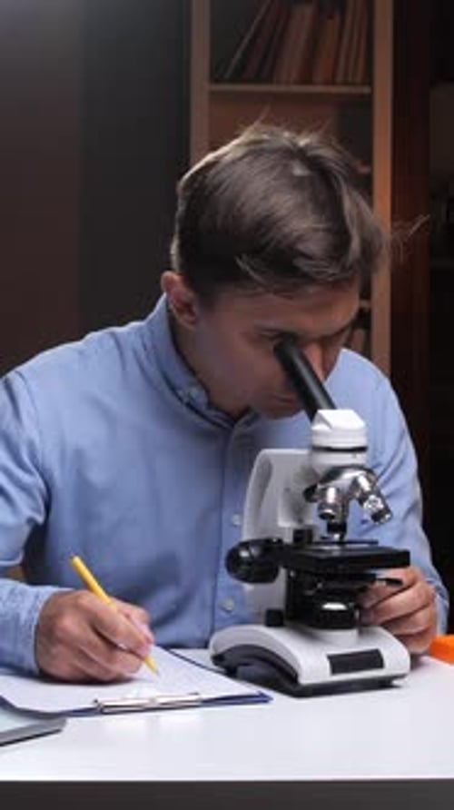Vertical Video Scientist Analyzing Sample Using Microscope and Taking Notes in Laboratory