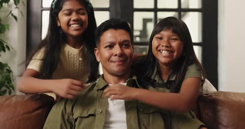 Happy Father Sitting with Two Daughters Hugging Him