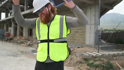 O construtor capataz sorridente se alegra com seu salário dançando em um canteiro de obras com um telefone