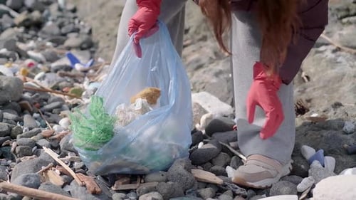 Woman Cleaning Up Trash on Rocky Beach