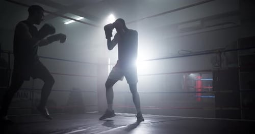 Silhouetted Boxers Sparring in Smoky Boxing Ring