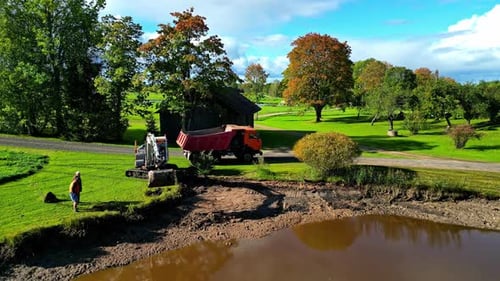 Excavator Loading Dump Truck with Dirt by Pond
